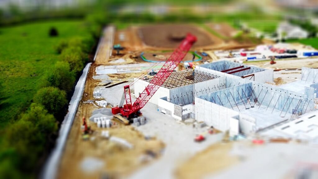 Arquitectura Rollon Contacto Madrid - Aerial view of a construction site with a red crane amidst green fields and concrete buildings.